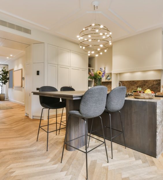 a kitchen and dining area in a house with wood floors, white cabinets, gray bar stools and marble counter tops