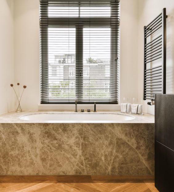 a modern bathroom with wood flooring and marble bathtub in the tub is surrounded by black shuttered windows